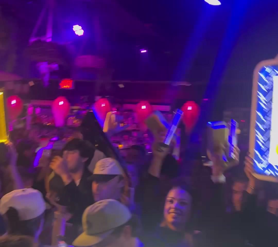 A packed club on a weekend night, sparklers and phone lights in the air
